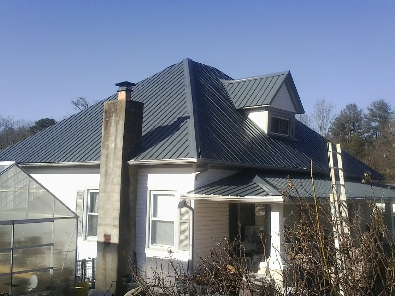 Dark blue standing seam metal roof on a white farmhouse with dormer — Slate & Tile Roof Repair by Roofing Brothers in Coolin