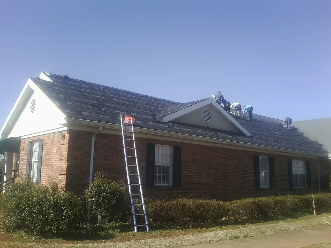 Crew tearing shingles off a brick ranch roof with a ladder set — Metal Roof Repair work by our crew in Coolin