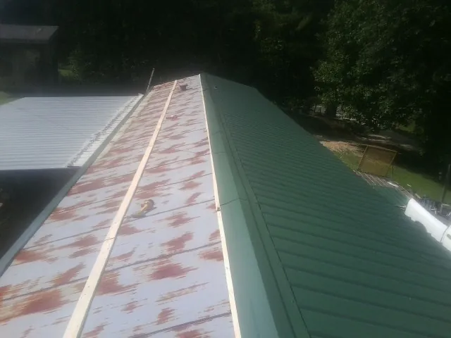 Old rusted panels beside newly installed green metal roofing — Wind Damage Roof Repair by Roofing Brothers in Coolin