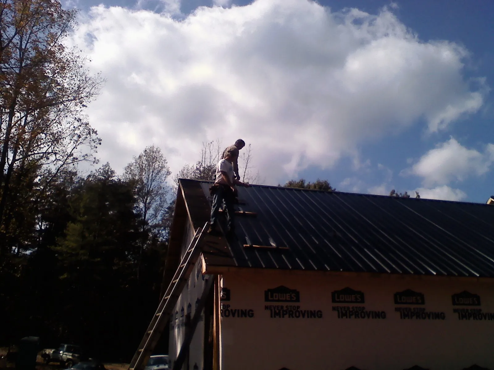 Roofer fastening dark metal panels high against a cloudy sky, from a Roof Inspection job in Coolin