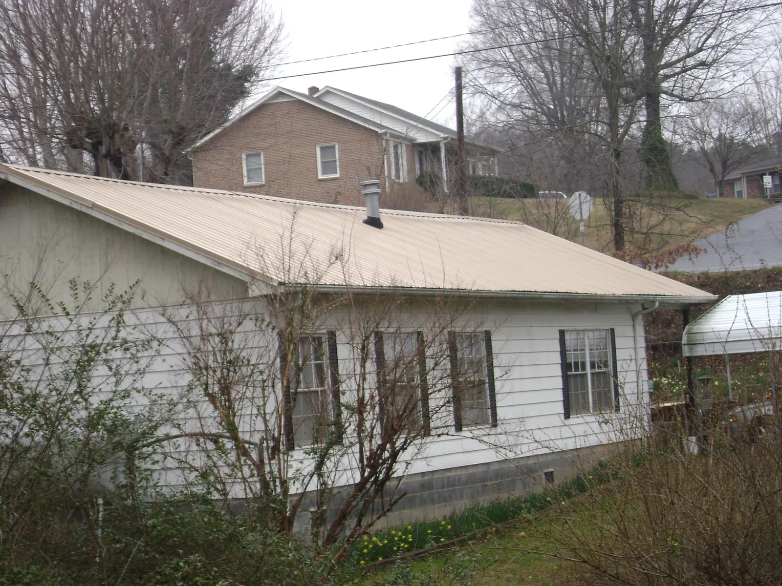 Tan metal roof on a white sided house set into a hillside — Commercial Roofing by Roofing Brothers in Coolin